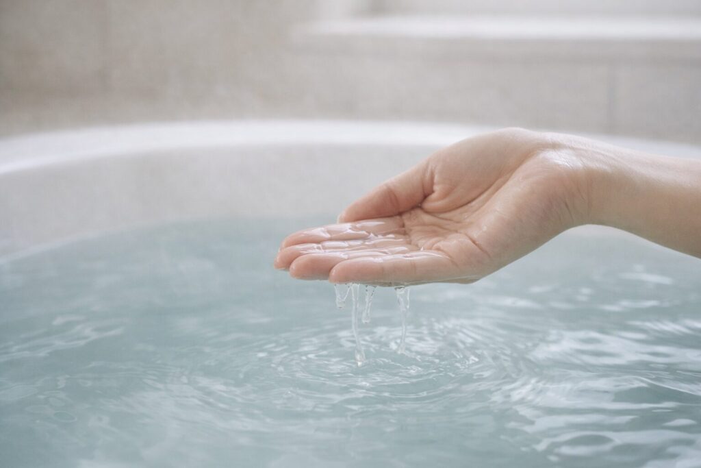 湯船のお湯を手ですくうアップ写真。 透明感のある水面と柔らかい光。